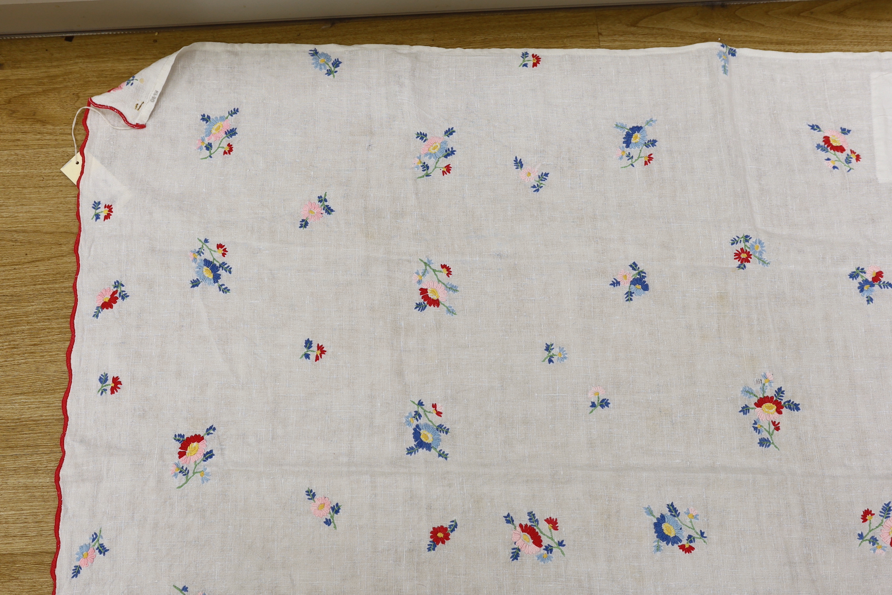 A 20th century woven linen panel, hand embroidered with scattered floral polychrome sprigs and a scalloped red buttonholed embroidered edge, possibly Swiss, 153 x 100cm